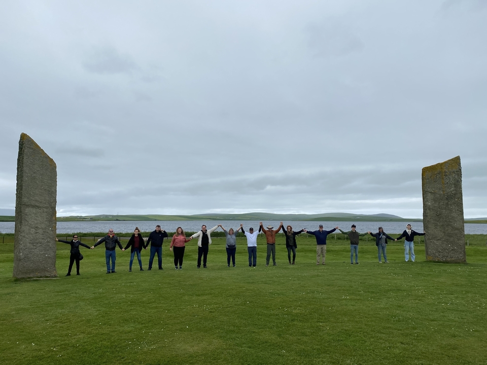 Group holding hands in a circle between two large standing stones.