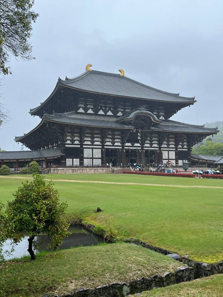 Une grande structure historique en bois avec des gens et de la verdure autour.
