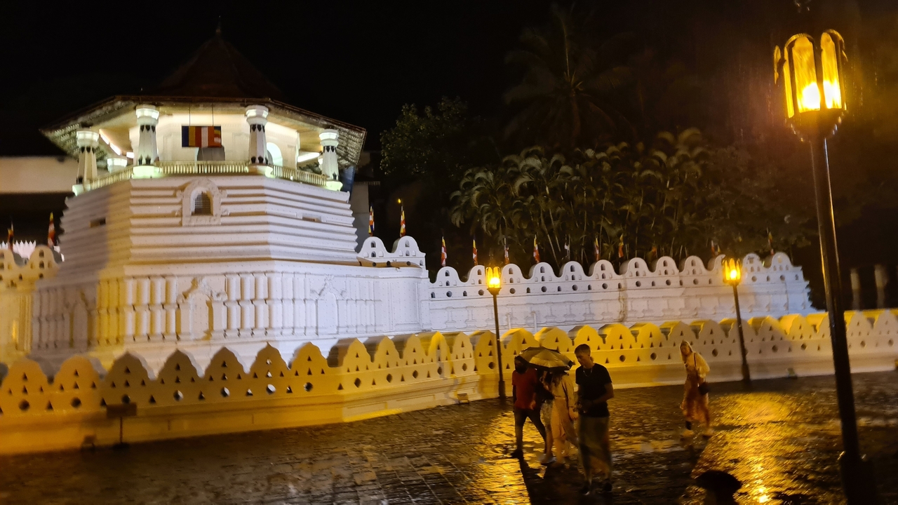 Un temple illuminé la nuit avec des gens qui passent.