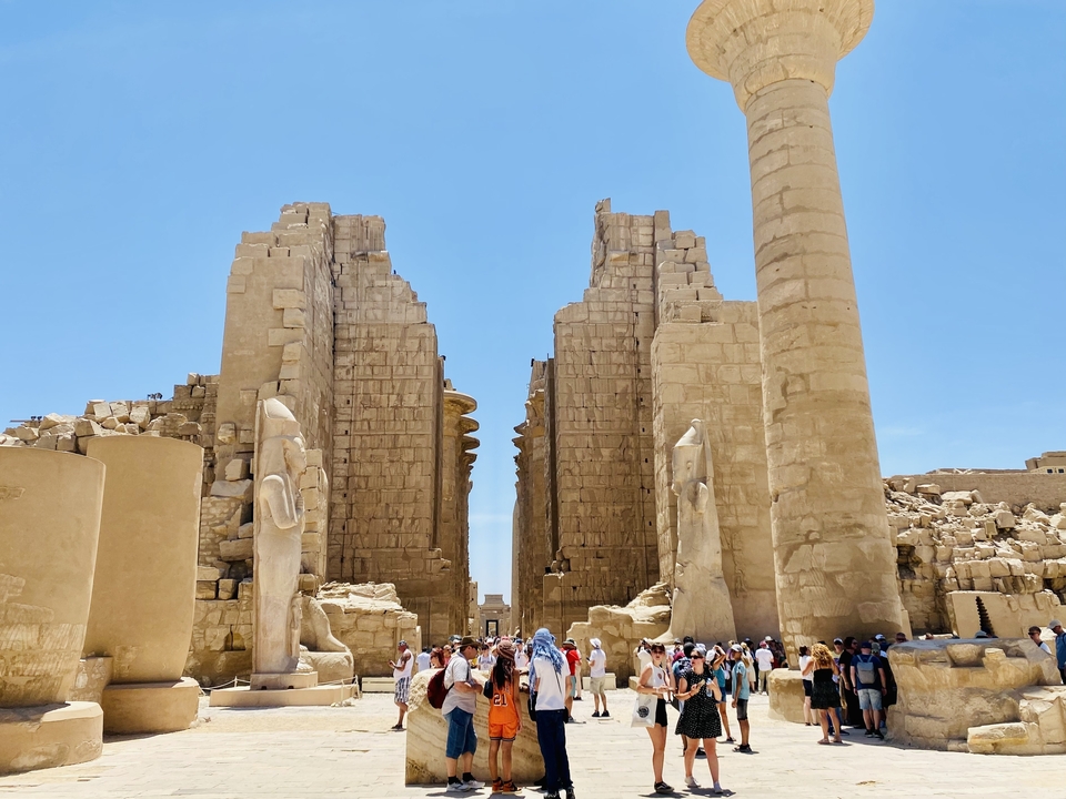 Ruines de temple avec de grandes statues et des touristes qui se promènent.