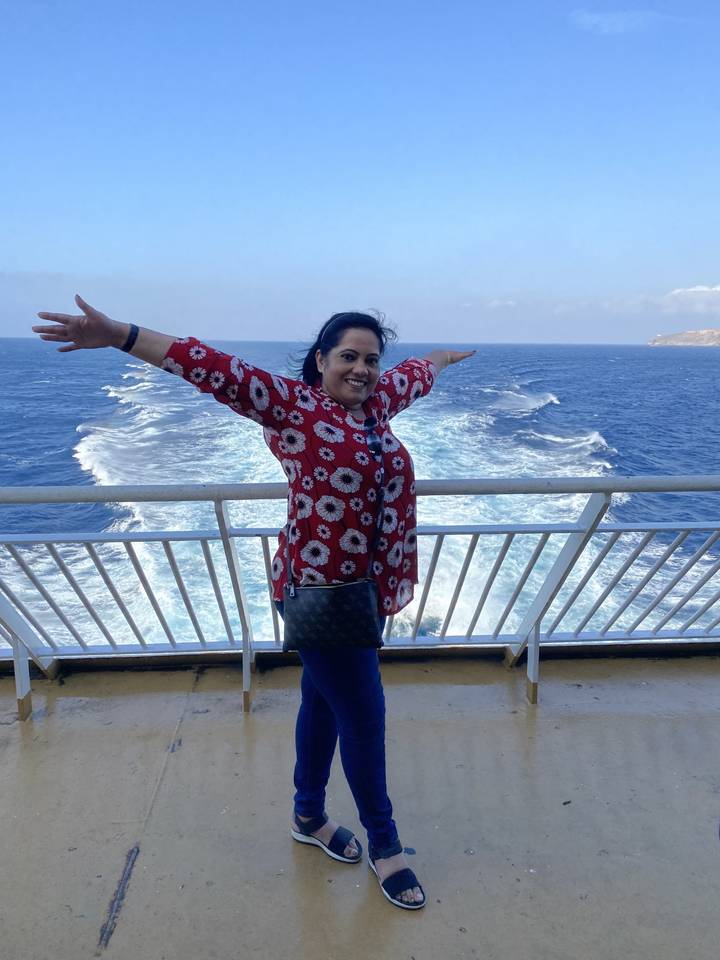 Une personne les bras écartés, debout sur un balcon donnant sur l'océan.