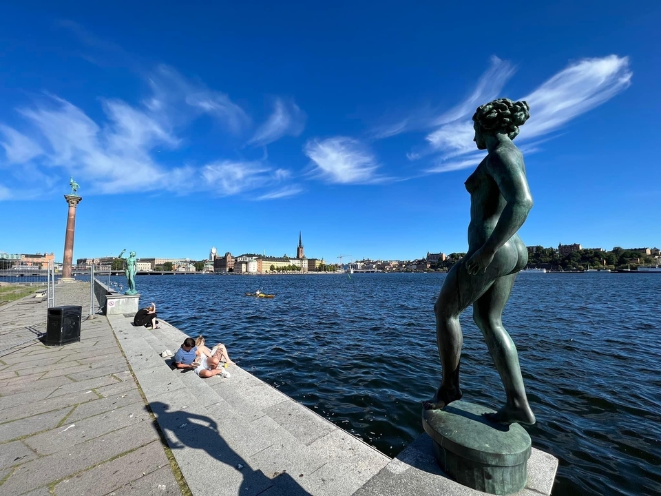 Vue au bord de l'eau avec une sculpture et horizon urbain.