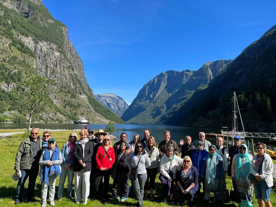Groupe de personnes debout devant un fjord pittoresque avec des falaises abruptes et une eau bleue.