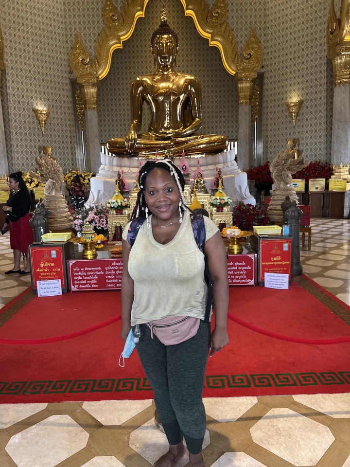 Une personne qui pose à l'intérieur d'un temple avec une statue de Bouddha couché.