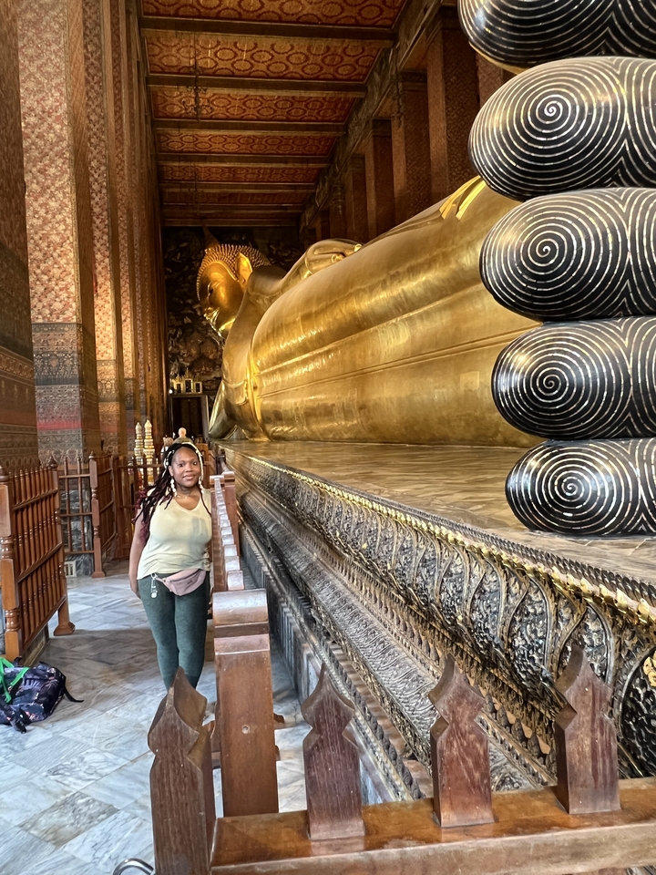 Une personne posant près d'une grande statue de Bouddha couché.