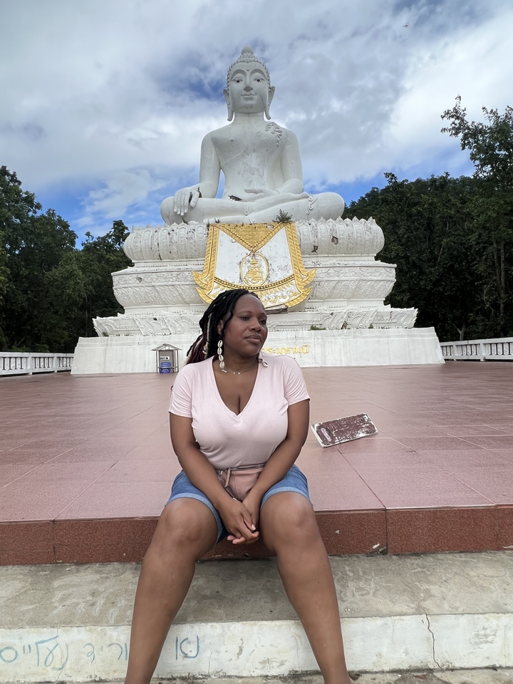 Une personne assise devant une grande statue blanche.