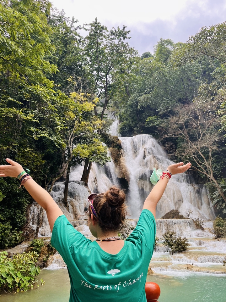 Person raising arms in excitement in front of a waterfall.