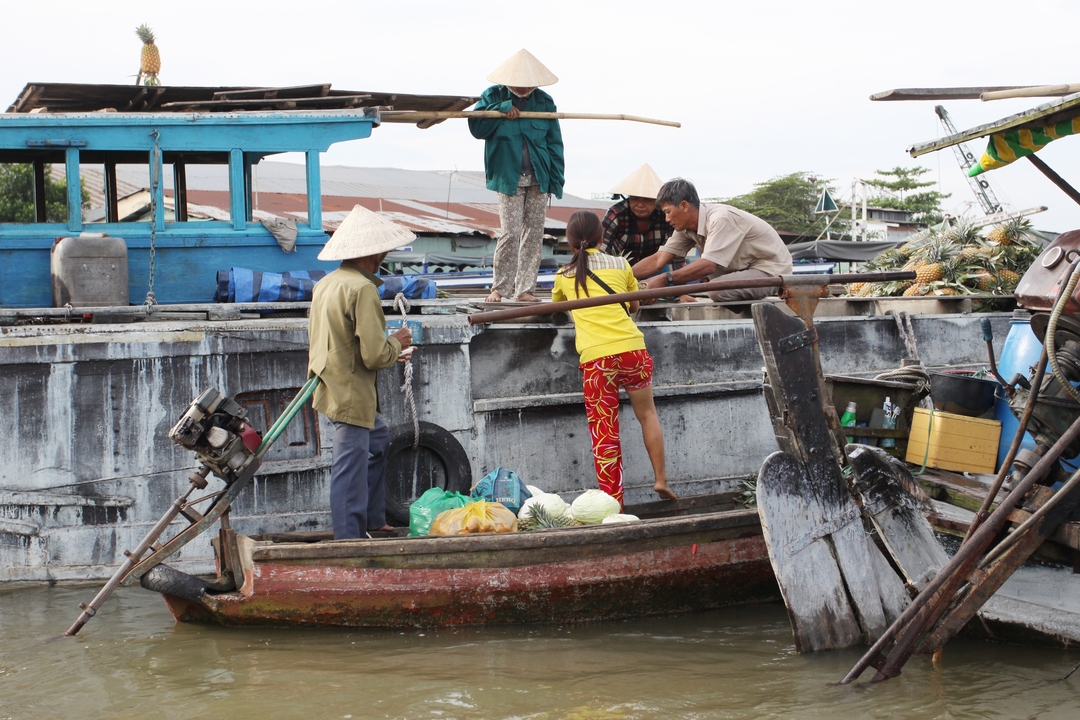 Vendors transferring produce between boats at a bustling river floating market