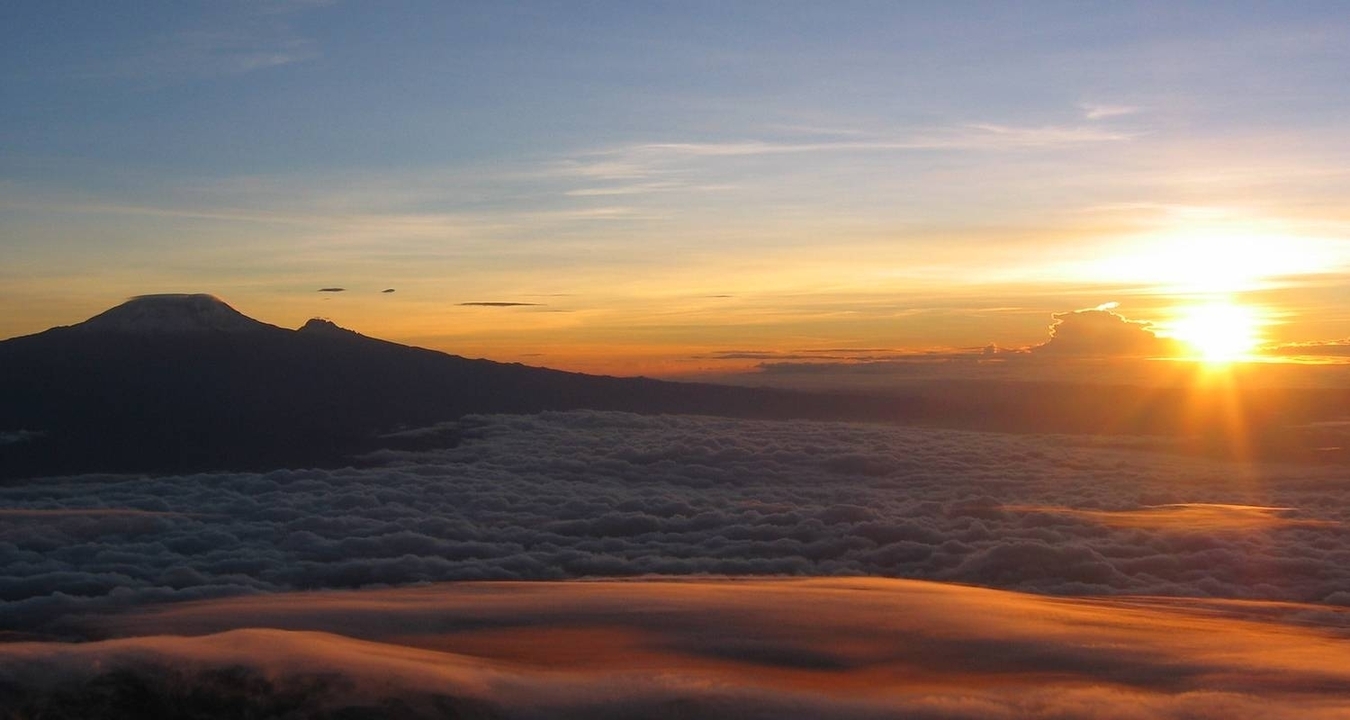 Lever de soleil sur un sommet de montagne entouré de nuages.