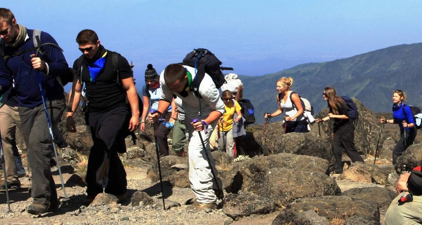 Groupe de randonneurs gravissant un terrain rocheux sous un ciel bleu éclatant.