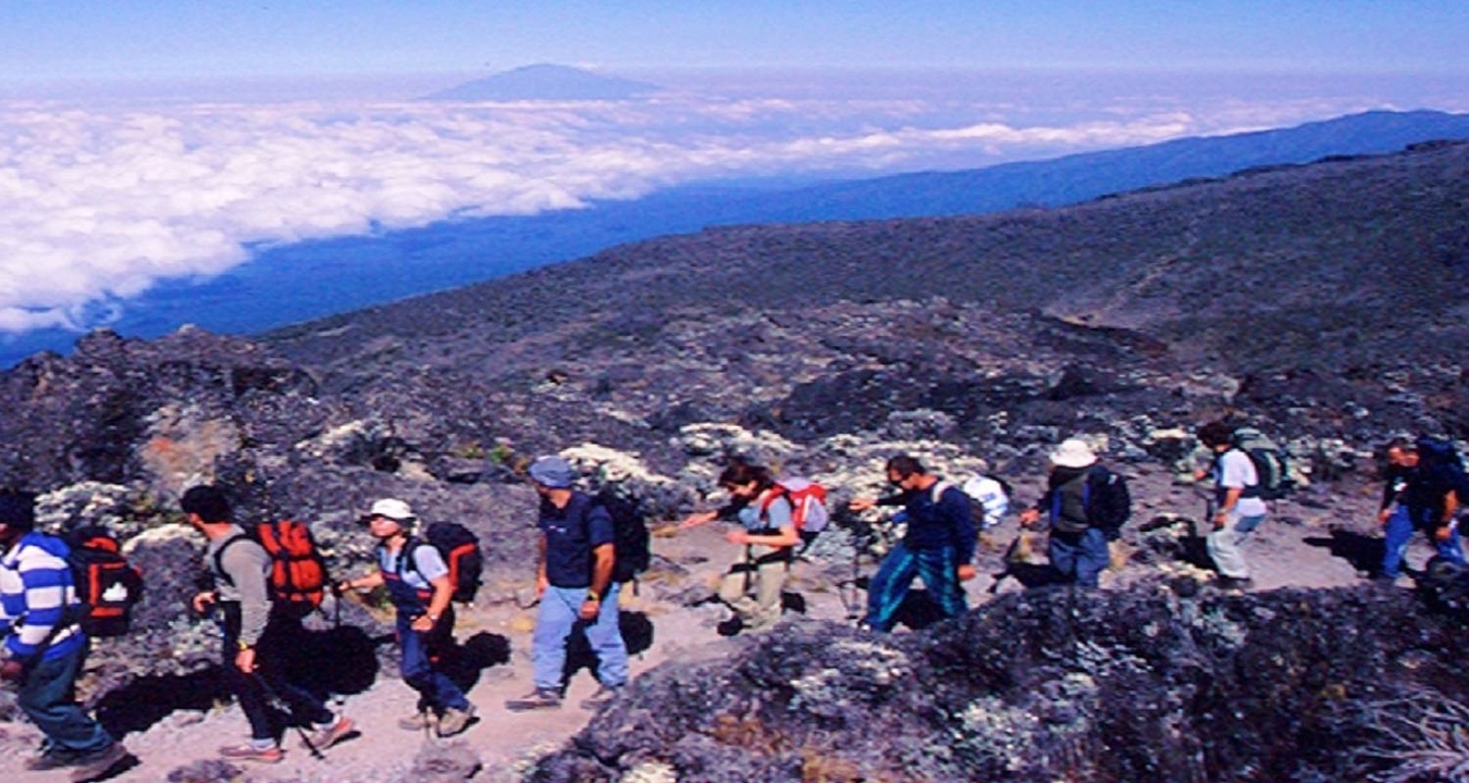 Randonneurs marchant le long d'un sentier avec des montagnes escarpées enveloppées de nuages.