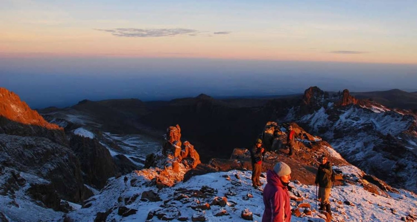Groupe de personnes au sommet enneigé profitant de la vue du lever de soleil.