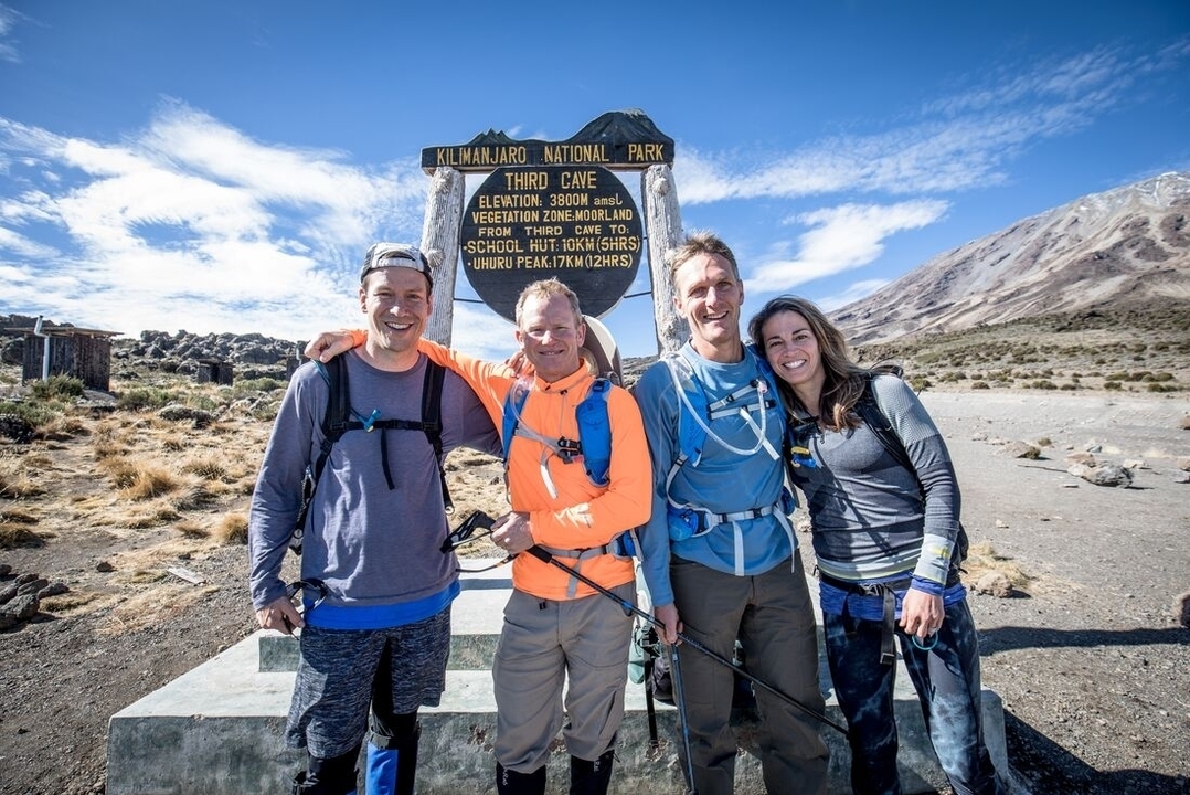 Quatre randonneurs souriants devant un panneau de grotte.