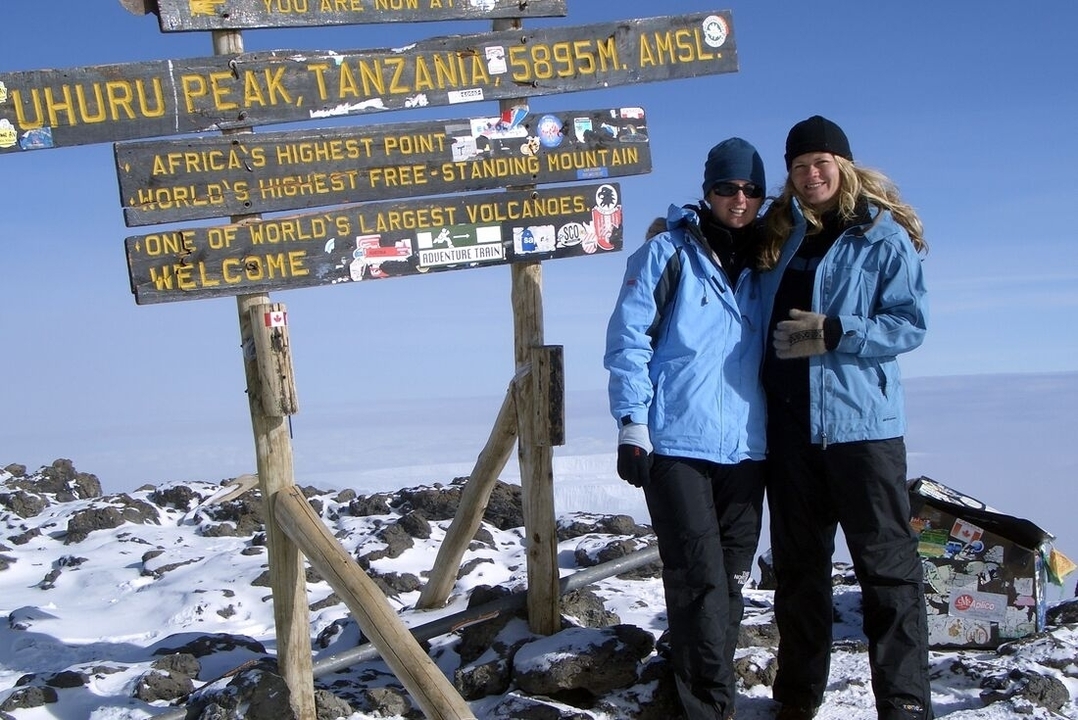 Deux personnes posant devant le panneau du sommet d'Uhuru Peak.