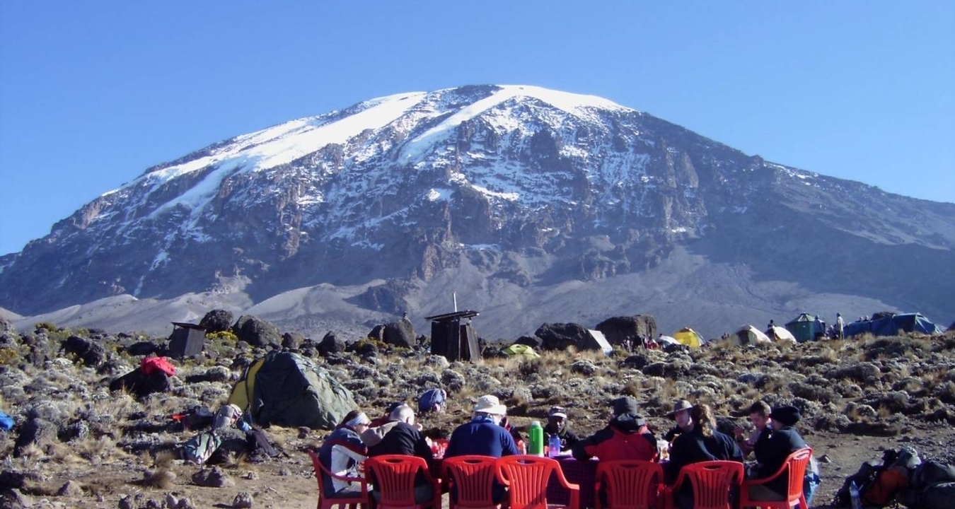 Un groupe dînant en plein air avec le mont Kilimandjaro en arrière-plan.