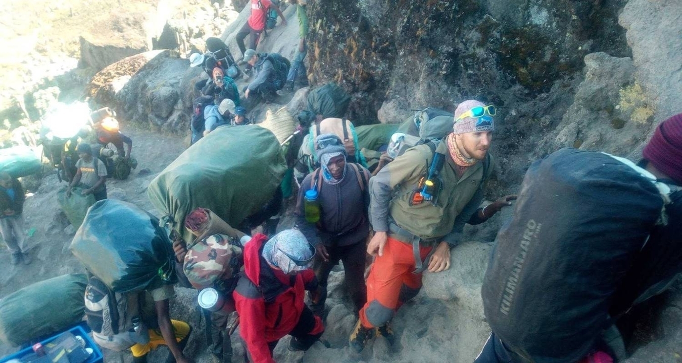 Des randonneurs gravissent un sentier de montagne avec des sacs à dos et de l'équipement.