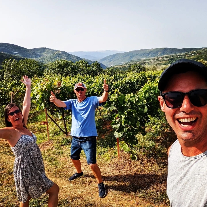 Groupe de personnes posant joyeusement dans un vignoble avec des collines verdoyantes luxuriantes.
