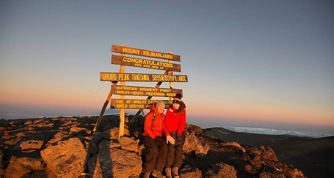 Deux personnes assises au sommet du Kilimandjaro pendant le coucher de soleil.
