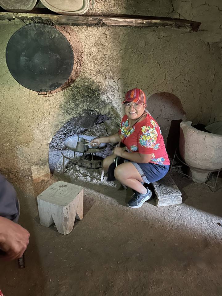 Personne agenouillée devant un petit foyer en pierre dans un cadre intérieur.