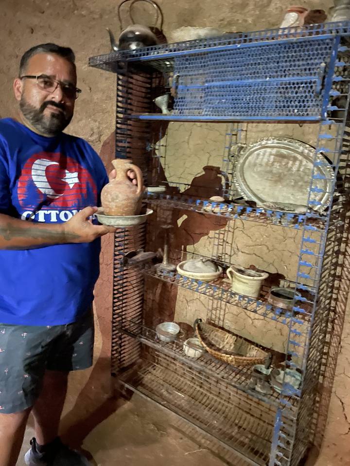 Personne tenant un objet en céramique près d'un mur rempli de poteries.