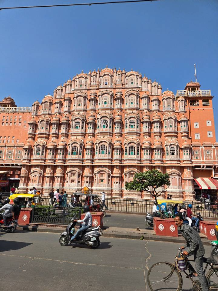 Façade rose d'un bâtiment historique avec des personnes et des véhicules devant.