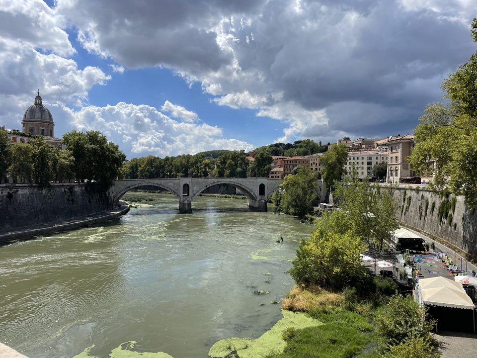 Pont de pierre sur une rivière avec des arbres et des bâtiments qui bordent les rives.