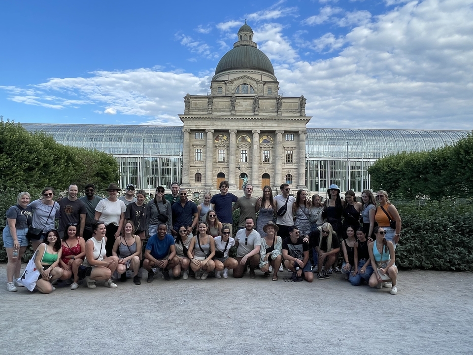 Large group posing in front of a grand domed government building and glass conservatory