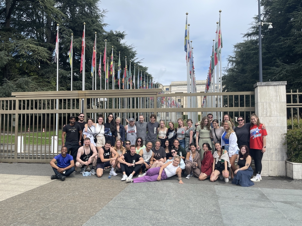 Group standing outside the gated entrance of the United Nations with multiple flags flying