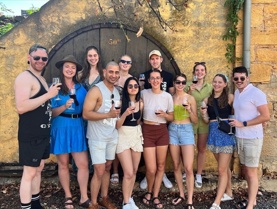 Group of young adults toasting wine outside a rustic stone cellar wall