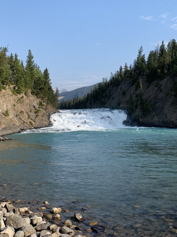Cascade tombant dans une rivière bordée d'arbres et de rochers.