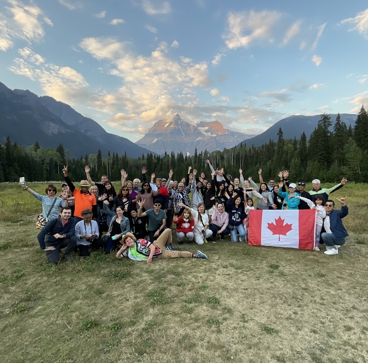Grand groupe de personnes avec un drapeau canadien dans une prairie pittoresque.