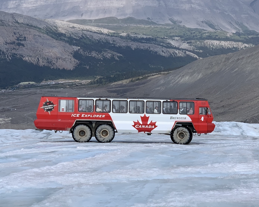 Véhicule Ice Explorer sur un glacier avec des montagnes au loin.