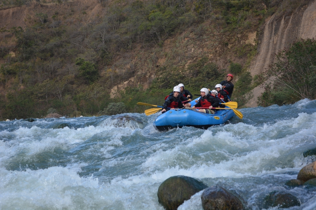 Groupe de personnes portant des casques et des gilets de sauvetage faisant du rafting sur une rivière avec des rapides.