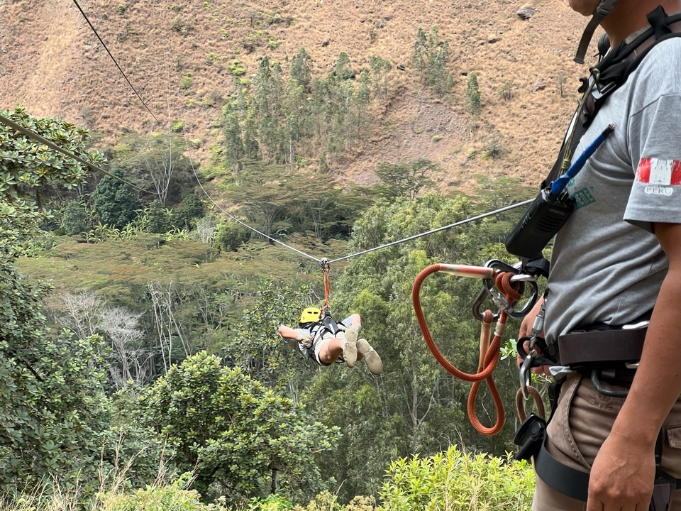 Personne faisant de la tyrolienne au-dessus d'une vallée boisée.