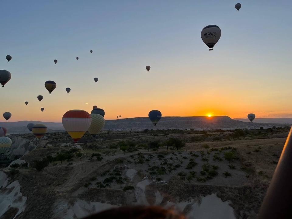 Plusieurs montgolfières au-dessus d'un paysage au lever du soleil.