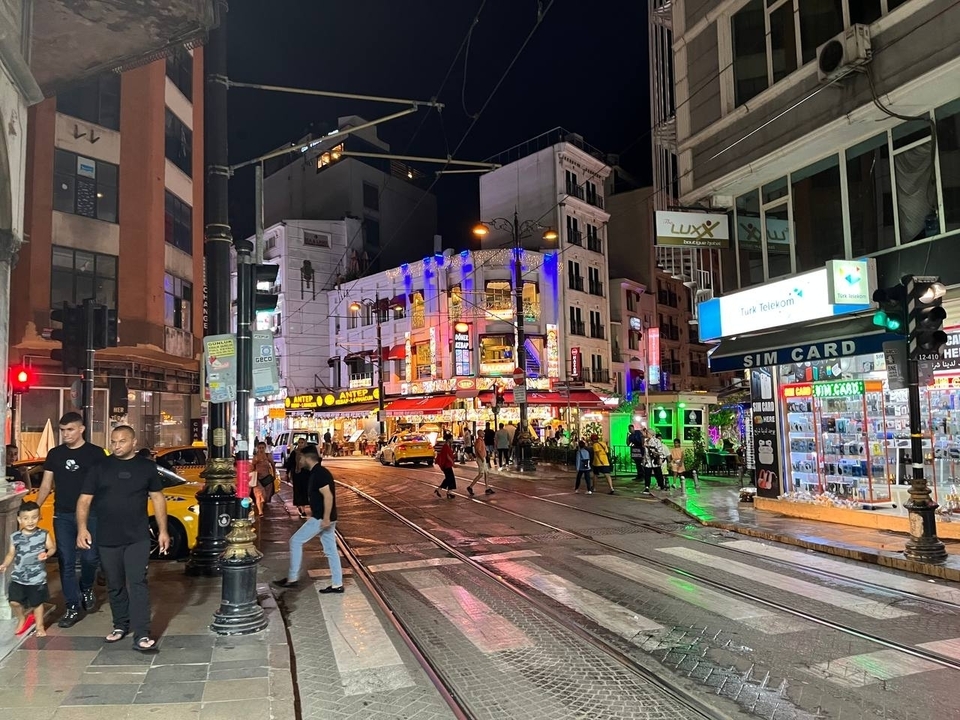 Scène de rue animée la nuit avec des lumières vives et des piétons.