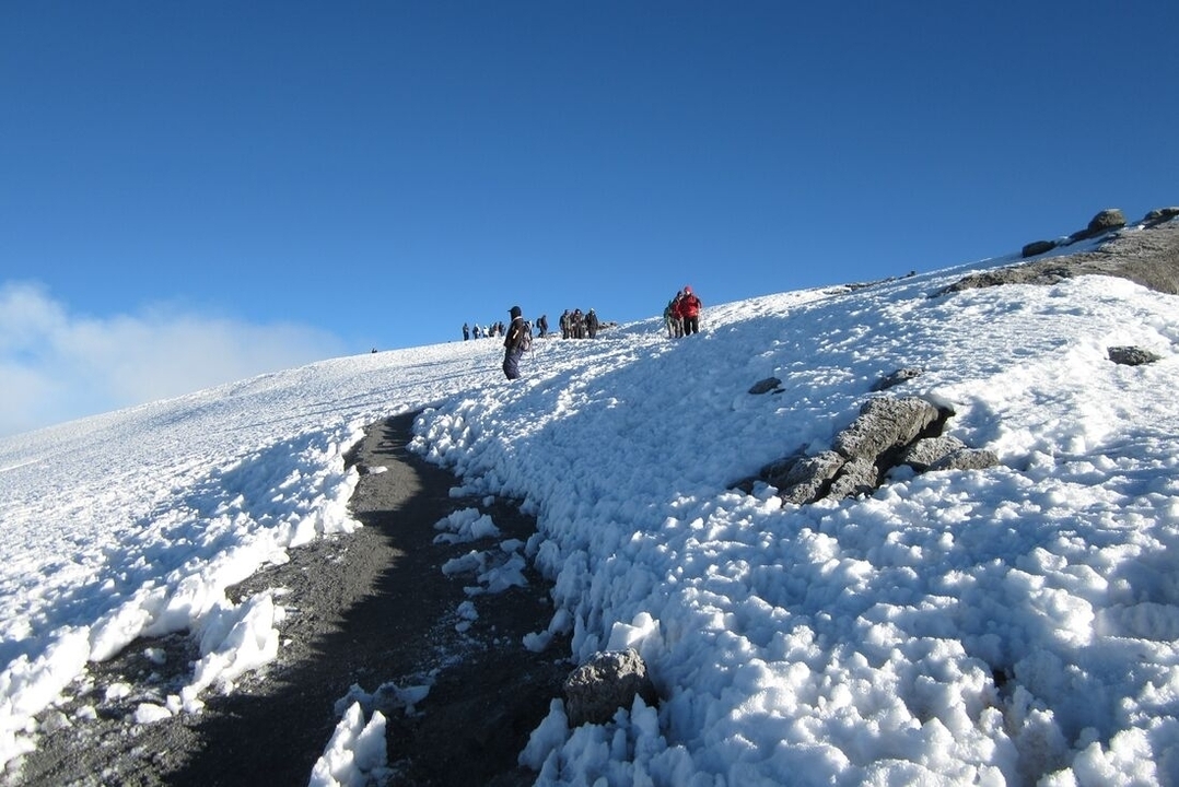 Randonneurs gravissant un sentier enneigé par une journée claire.