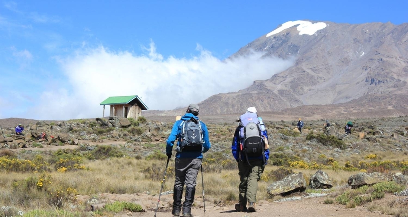 Randonneurs marchant vers une montagne enneigée avec une petite cabane visible.