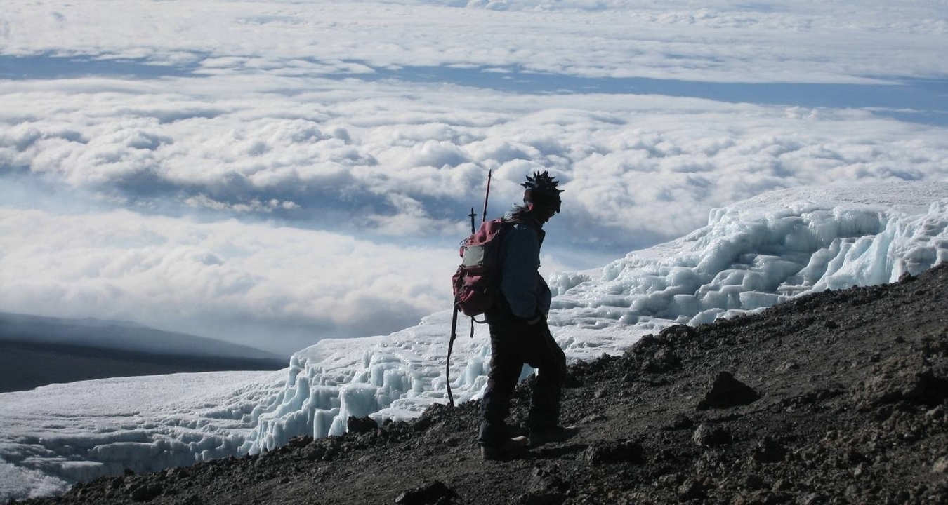 Personne marchant sur une crête de montagne enneigée avec des nuages en contrebas.