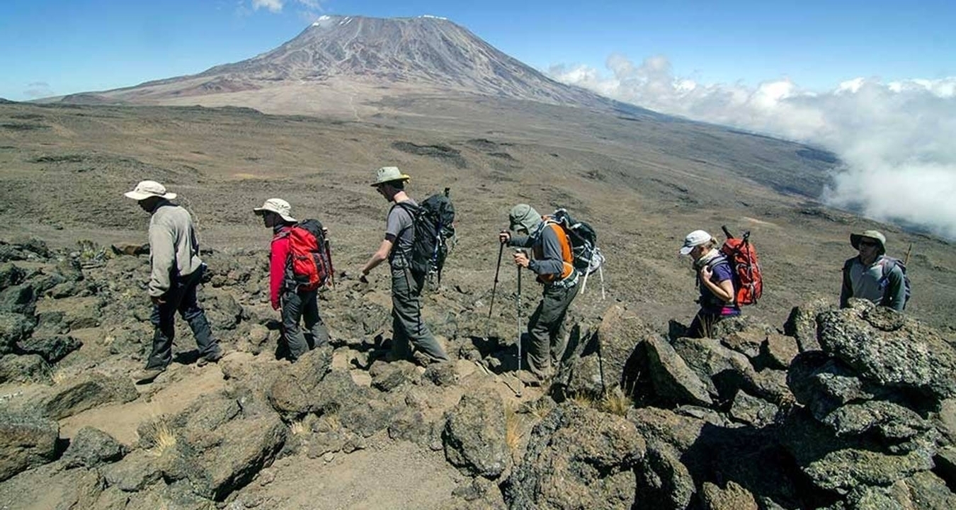 Randonneurs traversant un paysage rocheux avec une montagne en arrière-plan.