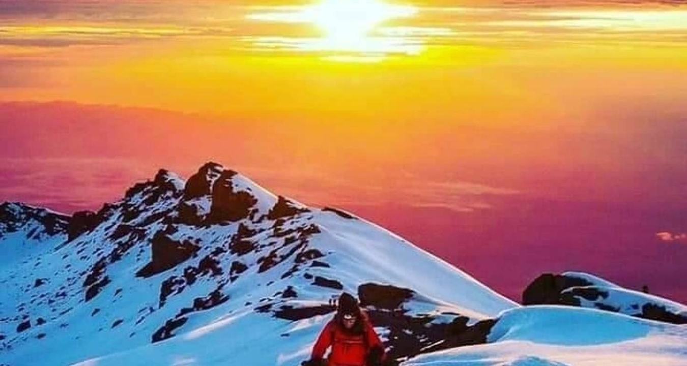 Personne escaladant une montagne enneigée pendant le coucher de soleil.