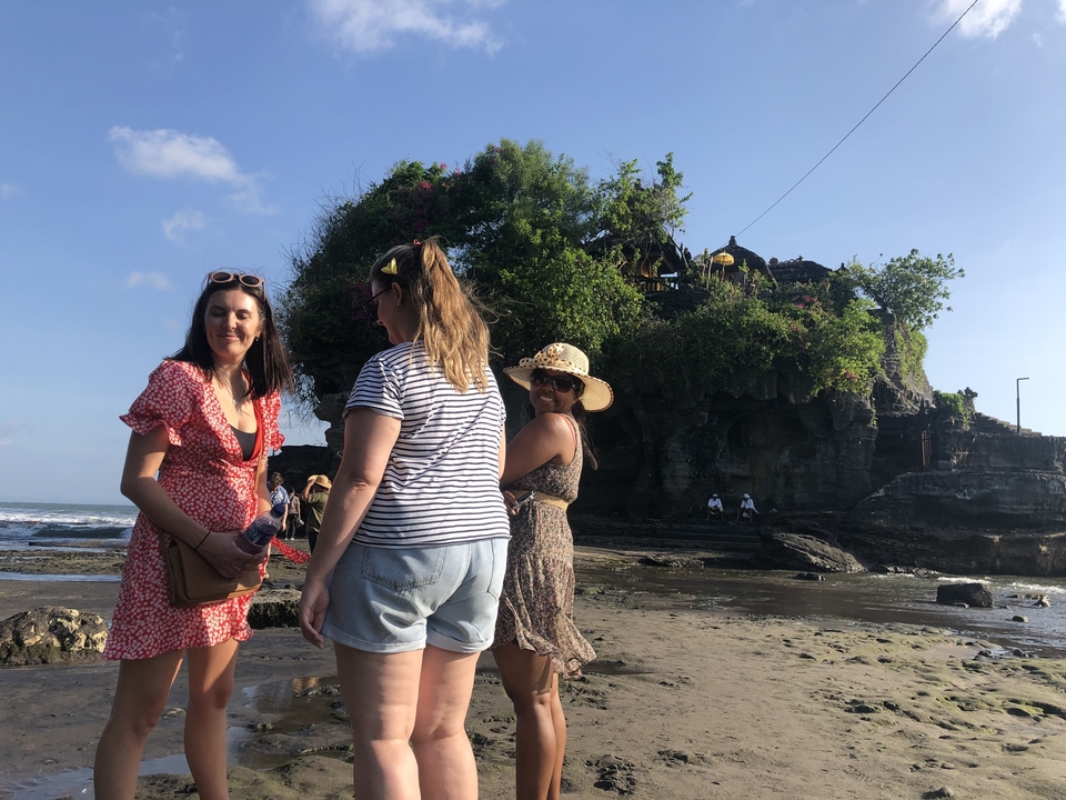 Des gens qui marchent sur une plage près de falaises avec une structure au sommet.