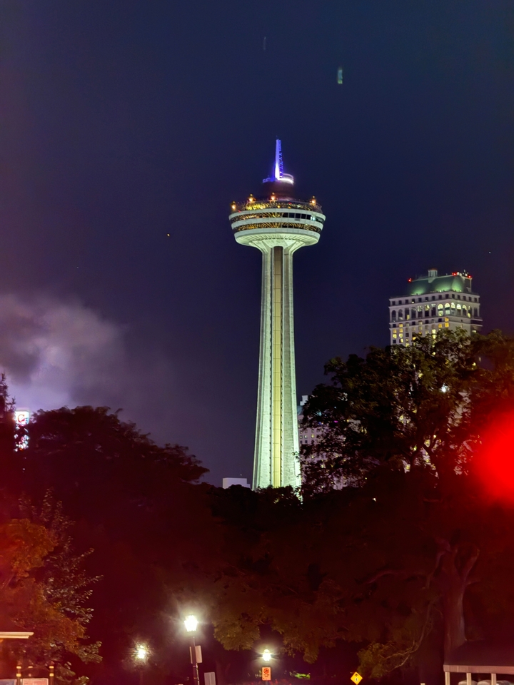 Tour Skylon illuminée la nuit, entourée d'arbres et de lumières.