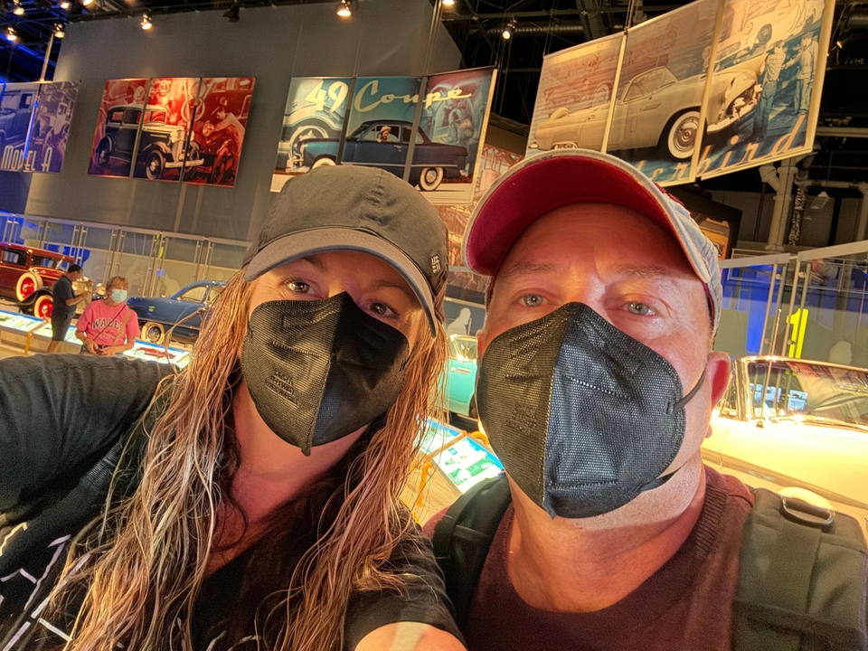 Deux personnes portant des masques dans un musée de l'automobile.