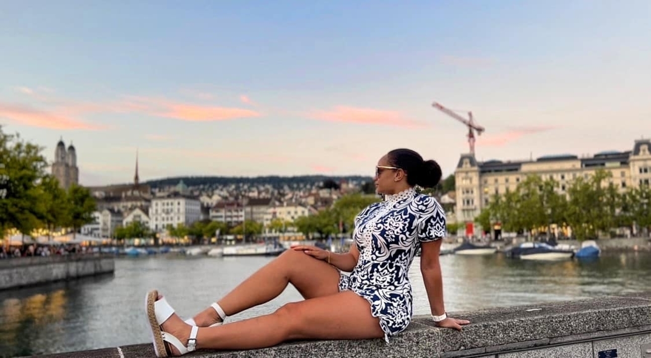 Femme assise au bord de la rivière à Zurich avec un ciel de coucher de soleil.