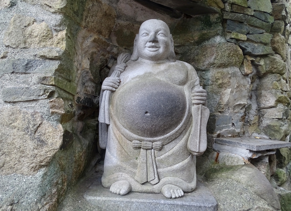 Statue de pierre d'une figure assise contre un mur de roche.