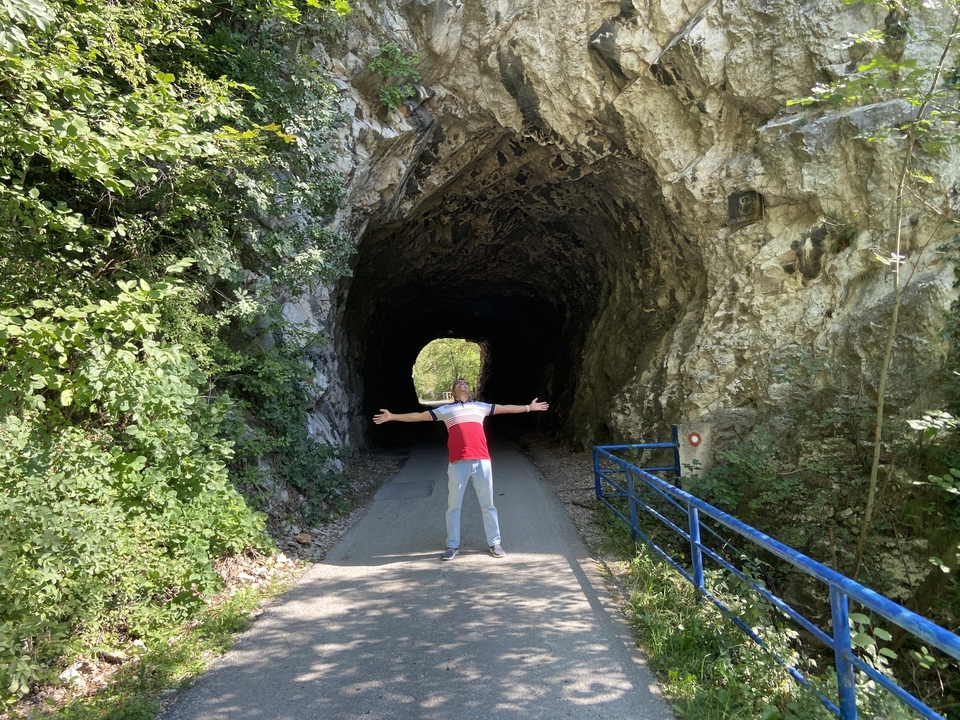 Person, die mit ausgestreckten Armen vor einem Tunneleingang steht, umgeben von felsiger Landschaft.