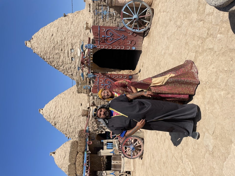 Deux personnes en vêtements traditionnels se tenant debout devant des structures en forme de dôme.