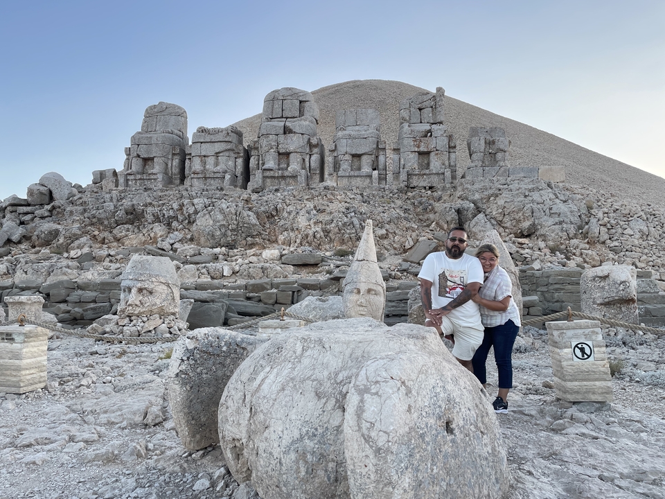 Deux personnes qui posent devant de grandes têtes de pierre antiques sur une montagne.
