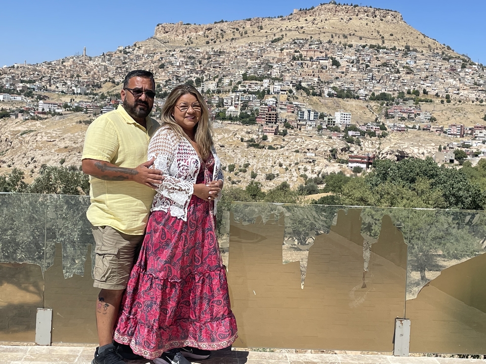 Deux personnes posant avec un paysage urbain et une colline en arrière-plan.